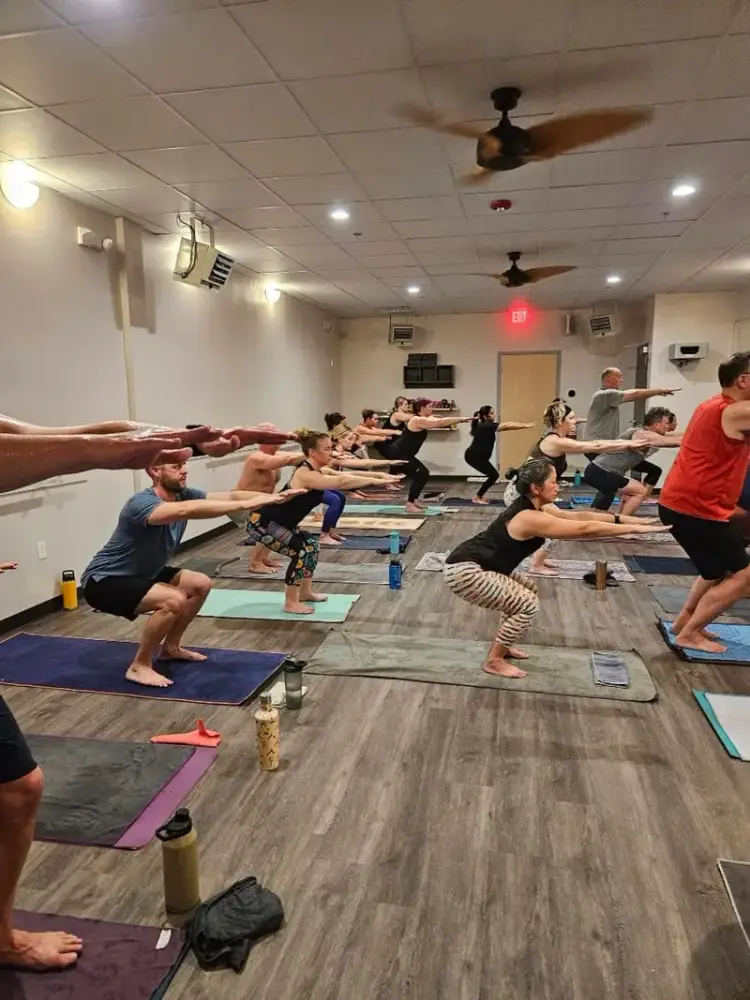 Chair pose with arms extended in a full hot yoga class
